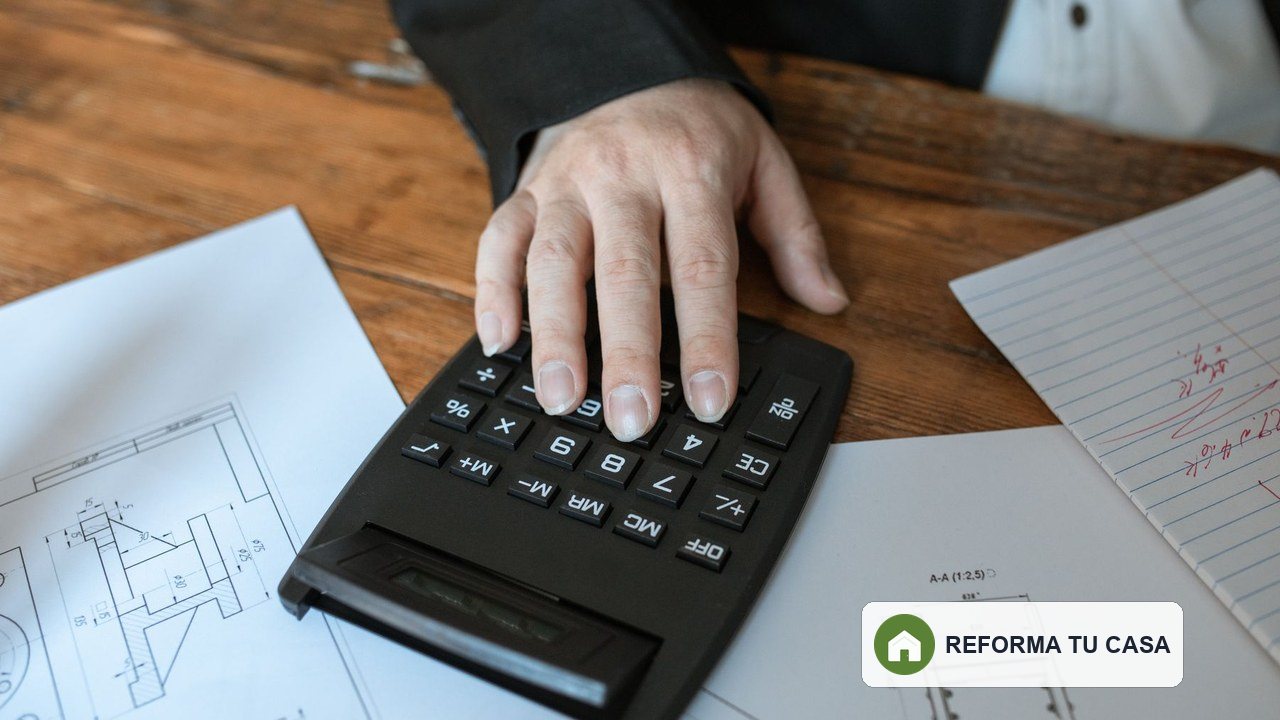 Mano usando una calculadora sobre planos de una reforma de vivienda