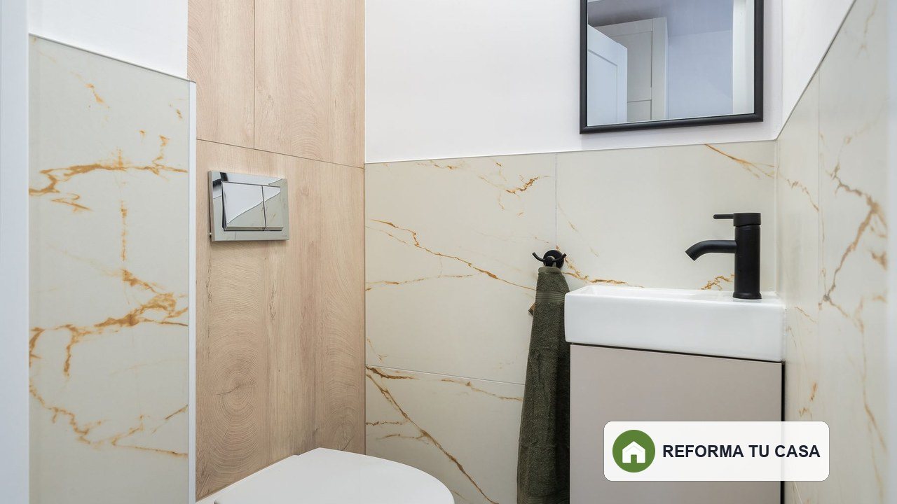 Baño compacto con revestimientos continuos, lavabo suspendido y encuentros visibles