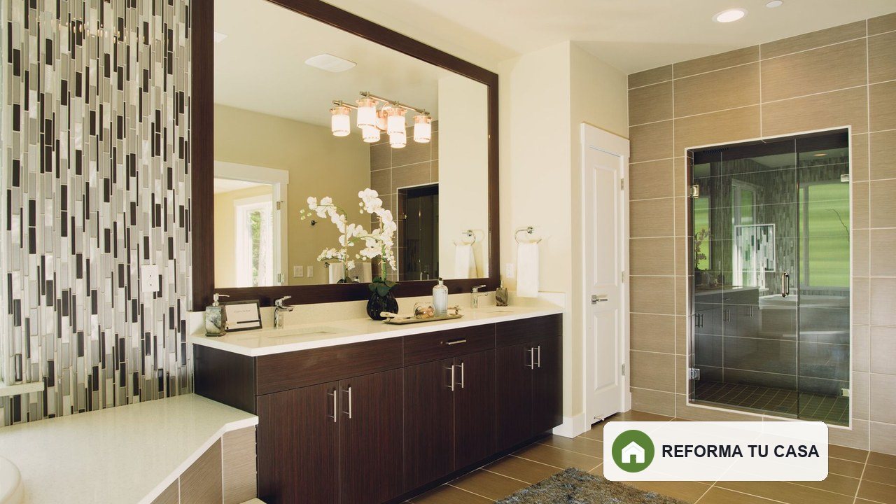 Baño renovado con mueble de madera, espejo amplio, ducha acristalada y revestimiento decorativo